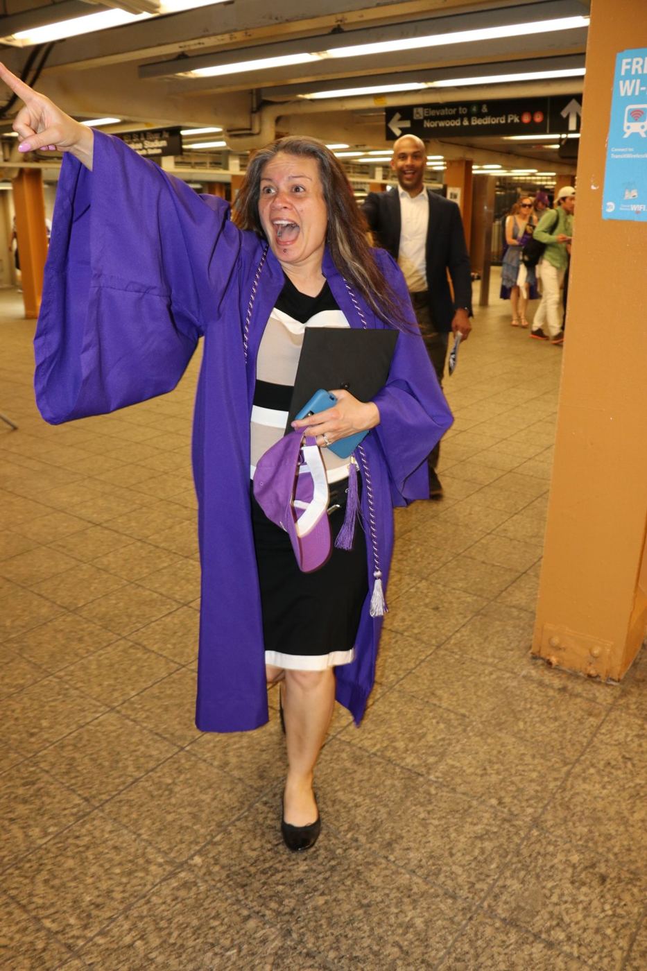 Gwen in her graduation gown, pointing and celebrating in the subway