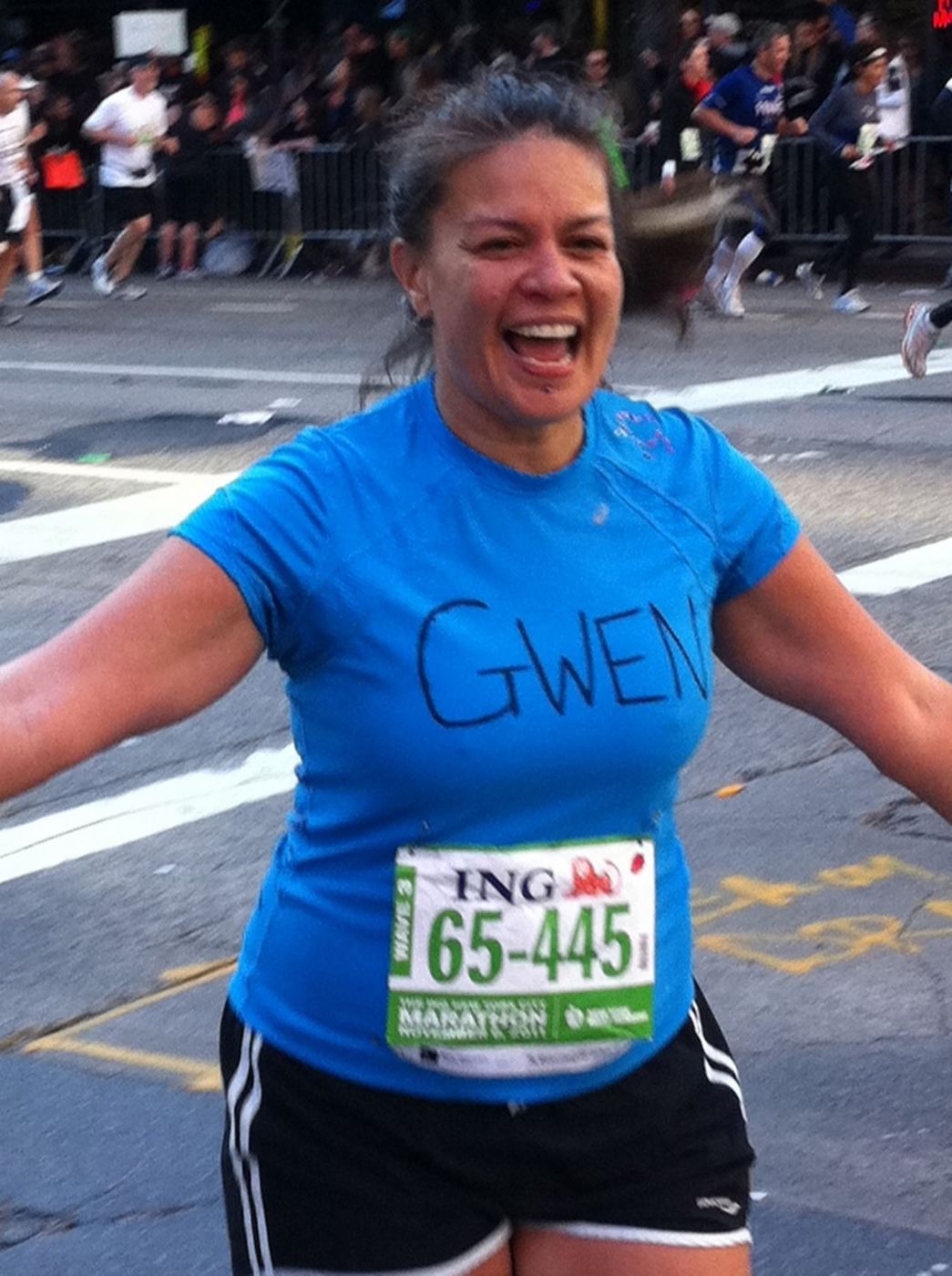 Gwen running the New York City Marathon in a blue shirt with GWEN written on it, arms wide